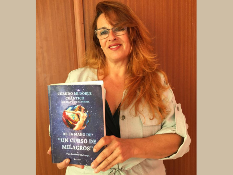 A una mujer con cabello rojo sosteniendo un libro titulado "Cuando mi doble cuántico me hace milagros". La portada del libro muestra un personaje en una escena misteriosa.
