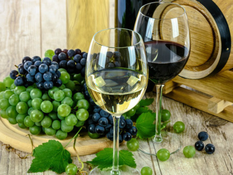 Uvas y vino en copas sobre una tabla de madera con un barril de fondo.