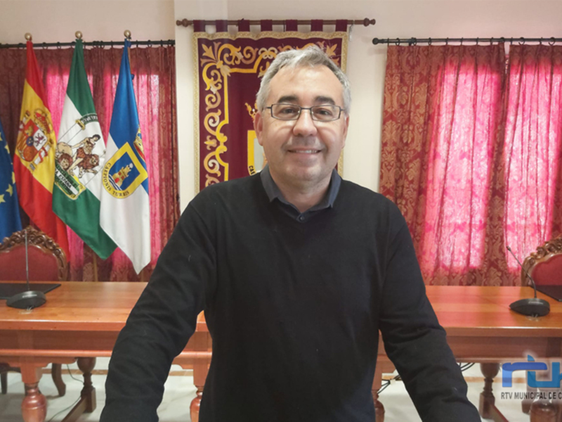 Persona sonriente en un despacho con banderas y cortinas rojas.