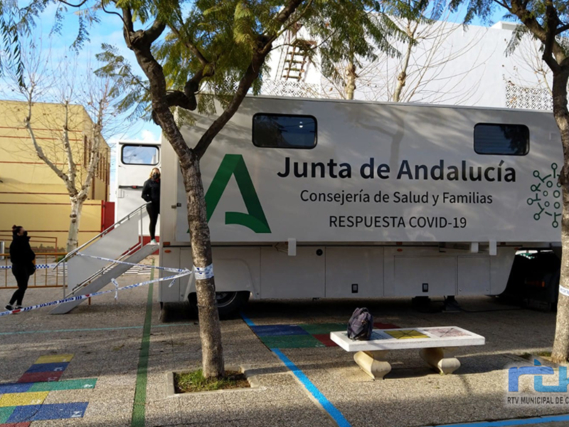 Un autobús móvil de la Junta de Andalucía con la etiqueta 'Respuesta COVID-19' en un entorno urbano, con una persona caminando cerca y una señal de precaución en el suelo.