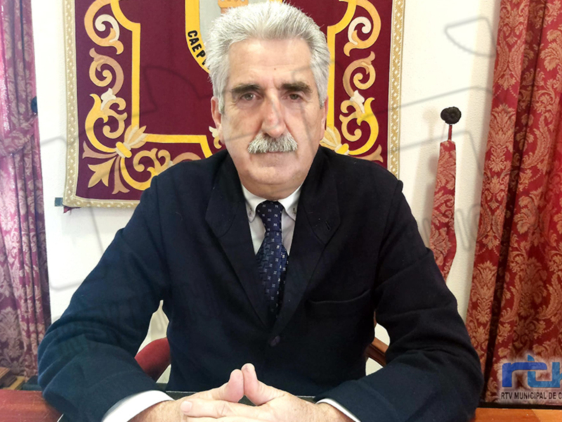 El presidente de la República, vestido con un traje oscuro y corbata, se encuentra sentado frente a una mesa. El fondo muestra un tapiz con símbolos y letras doradas, junto a cortinas rojas.