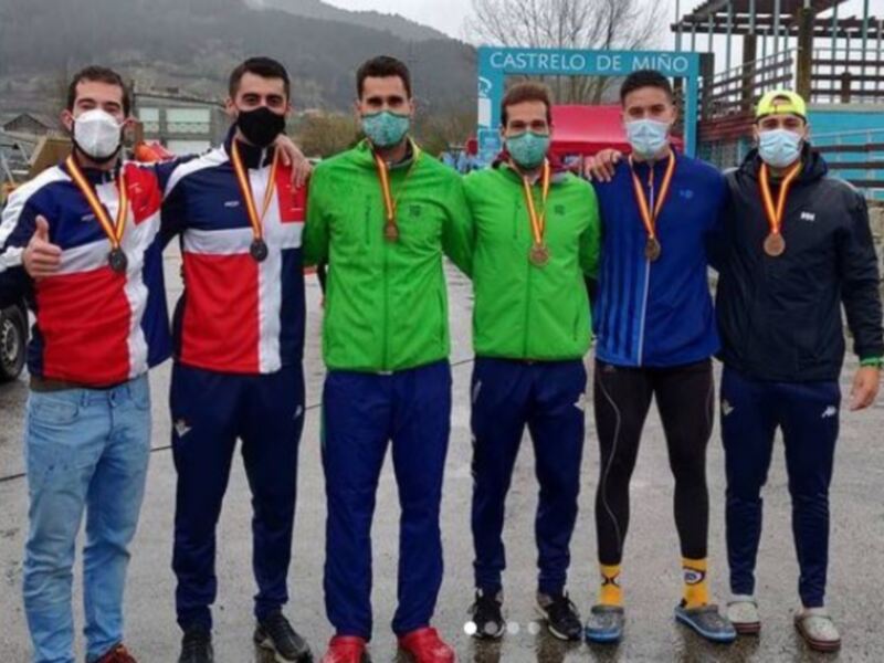 Un grupo de atletas posa con sus medallas en una carretera, con un cartel que dice 'Castrello de Mino' al fondo.