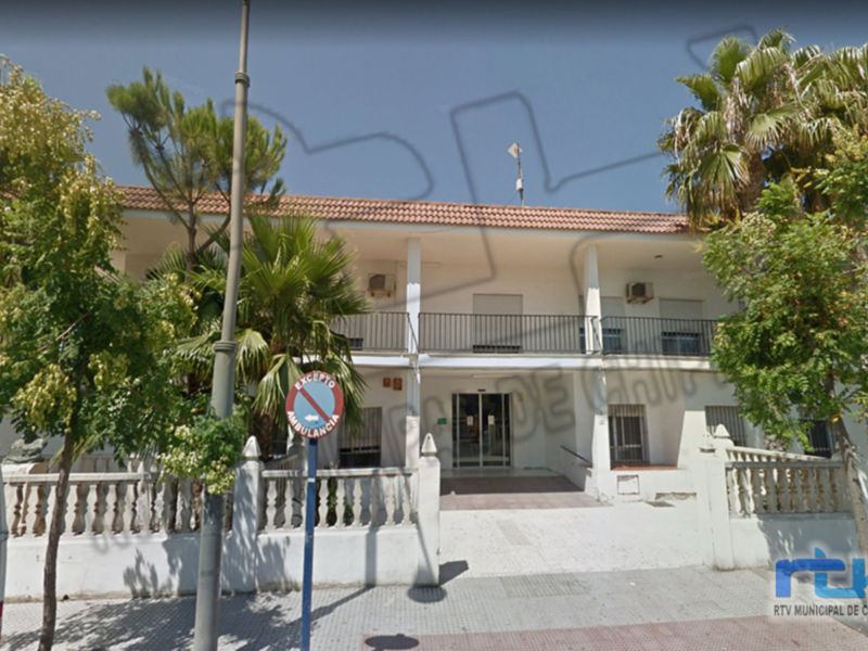 Fachada de un edificio con terraza y toldo, rodeado por árboles y una calle.