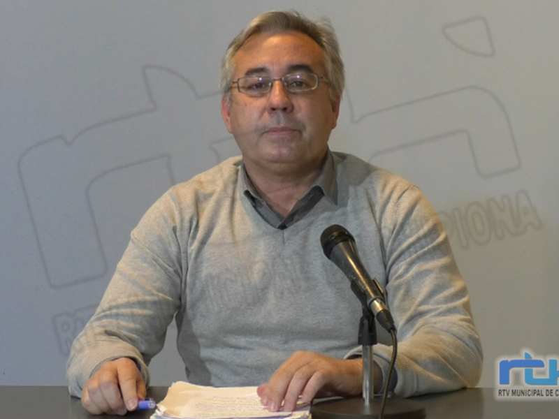 Un hombre con una camisa gris y gafas de lectura está sentado en frente de un micrófono, mientras sostiene una hoja de papel. La imagen tiene un fondo con formas geométricas y el logo "RTV.MUNICIPAL.DE.CHIPIONA" en la esquina inferior derecha.