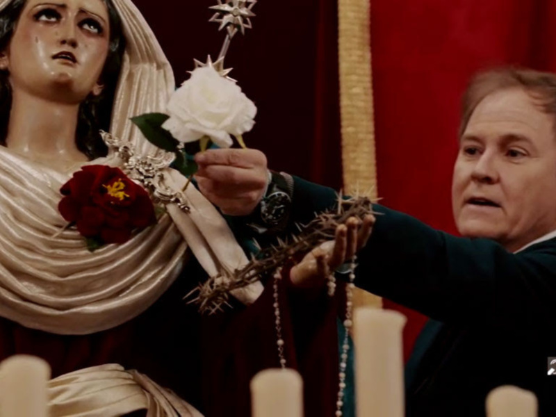 Una figura religiosa con una corona de espinas y un rosario, mientras un hombre la observa con atención.