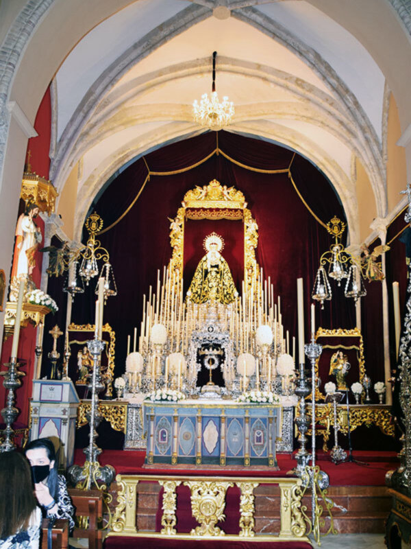 Interior de una iglesia con arcos y techos altos, estatuas religiosas, candelabros y un altar grande con flores.