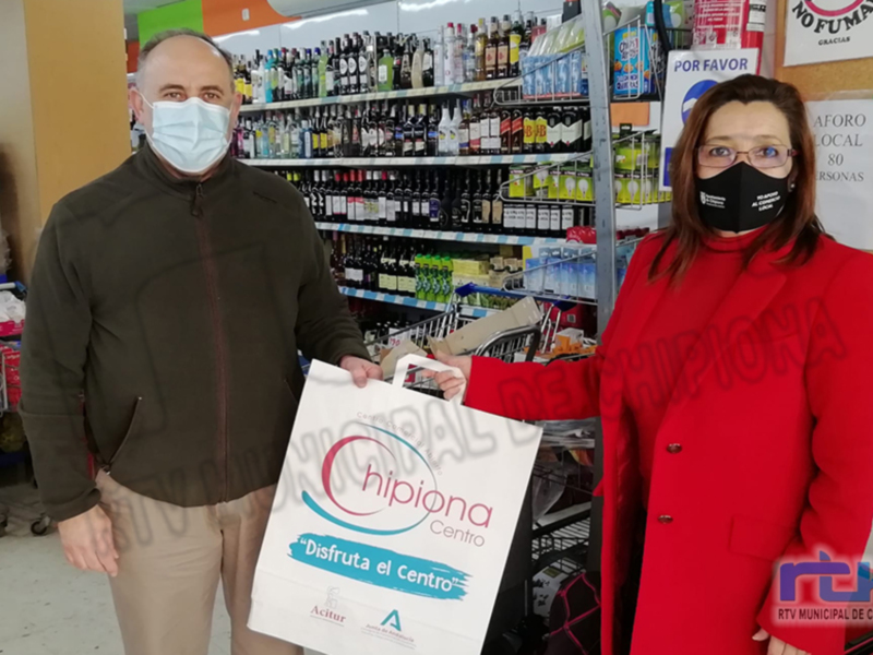 Dos personas con mascarillas posan en un supermercado con un paquete de la campaña "Disfruta el Centro" de Chipiona.