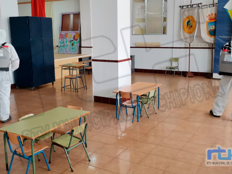 Imagen de una escuela desinfectada, con dos personas en trajes protectores. Muebles vacíos y decoraciones escolares visibles.