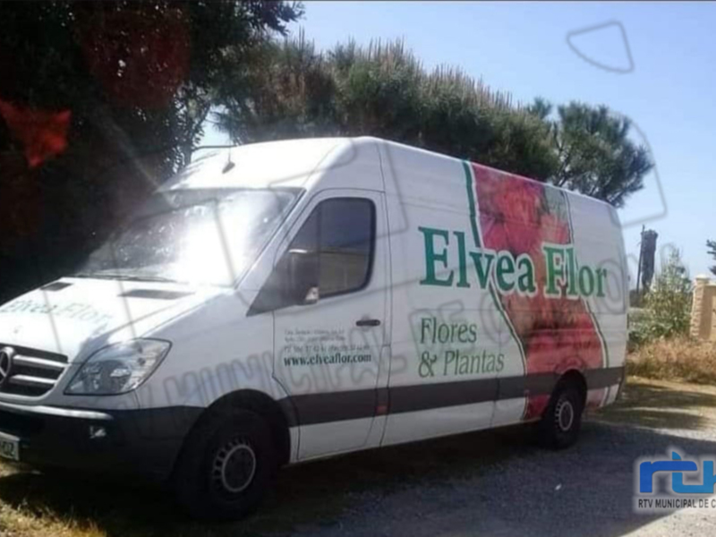Una camioneta blanca de Mercedes-Benz con publicidad de Elvea Flor. La imagen muestra un paisaje soleado con árboles y una cerca en el fondo.