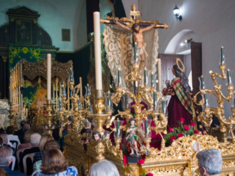 Interior de una iglesia con altares dorados, figuras religiosas y flores rojas.