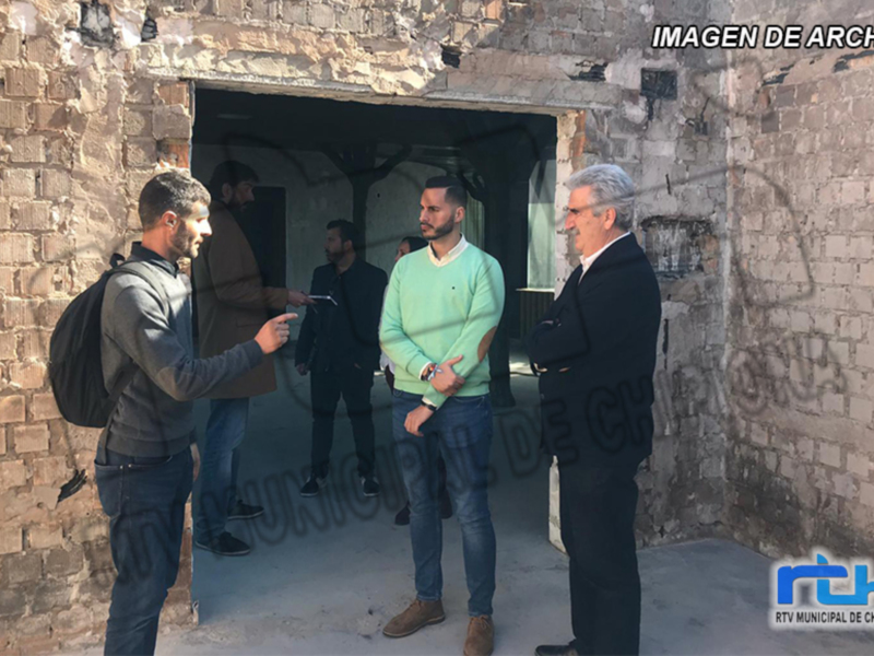 Un grupo de personas discuten en una entrada de un edificio con paredes de ladrillo. Algunos llevan mochilas y otros tienen objetos en las manos. La imagen parece ser de archivo, con texto que dice "IMAGEN DE ARCHIVO" y "RTV.MUNICIPAL.DE.CHIRONA".