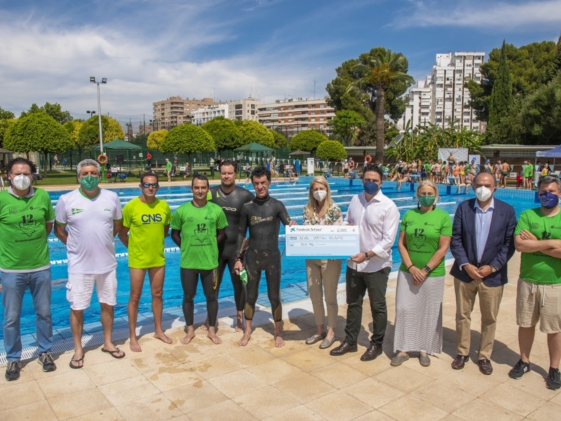 Equipo de nadadores y organizadores posando frente a una piscina con un cheque en la mano, celebrando un logro deportivo.