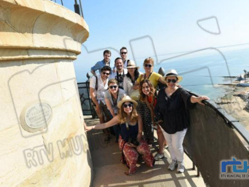 Grup de persones posant per una foto a una plataforma amb vista marina i una placa commemorativa.