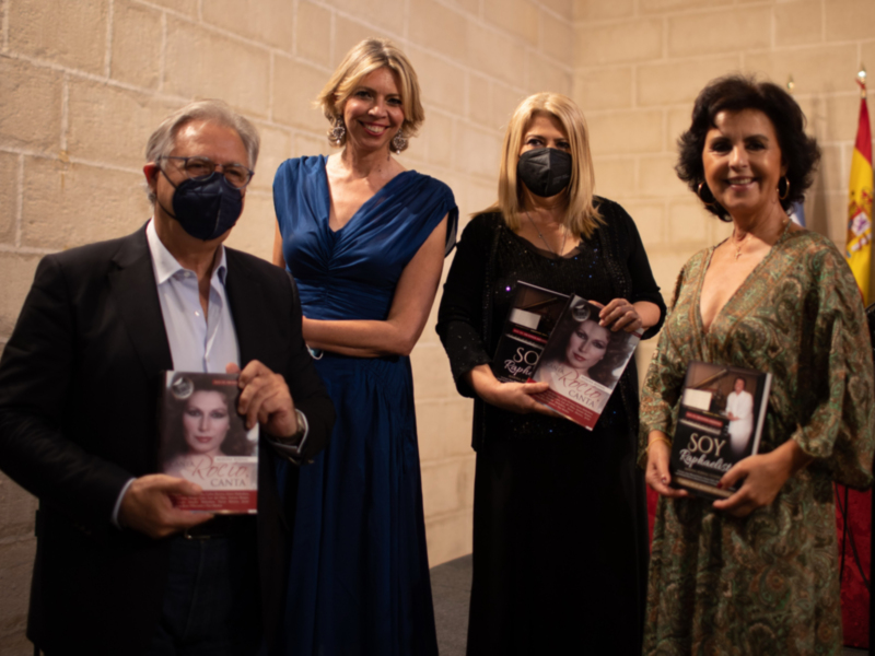 Una celebración con personas en trajes elegantes, sosteniendo libros titulados 'Soy Raphaela' y 'Soy Raphaela Canta'.