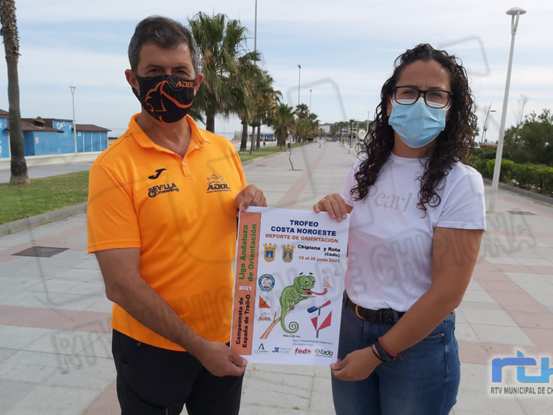 Dos personas sostienen un cartel con información sobre el Trofeo Costa Noroeste de Triatlón, en una calle con palmeras y edificios al fondo.
