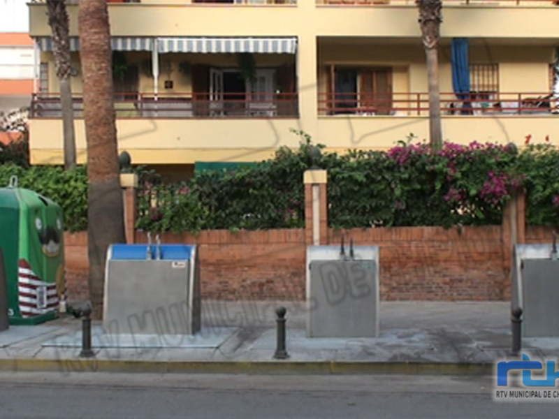Balcón de apartamentos con toldo azul y blanco, jardín con flores y plantas en primer plano.