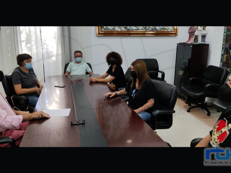 En una sala de reuniones, cinco personas se reúnen en torno a una mesa. La imagen muestra un ambiente formal con oficinas y decoración profesional, indicando una reunión de trabajo o negocios.