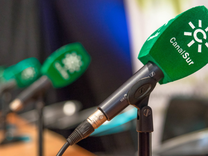 Microfones de mesa com capas verdes e logotipos de Canal Sur, indicando um ambiente de rádio ou televisão.