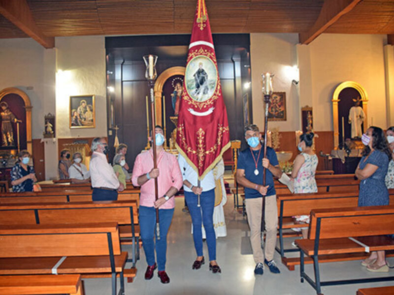 En una iglesia, personas con máscaras sostienen un escudo y un bastón. La imagen muestra una ceremonia religiosa con personas vestidas formalmente, posiblemente en un evento histórico o ceremonial.