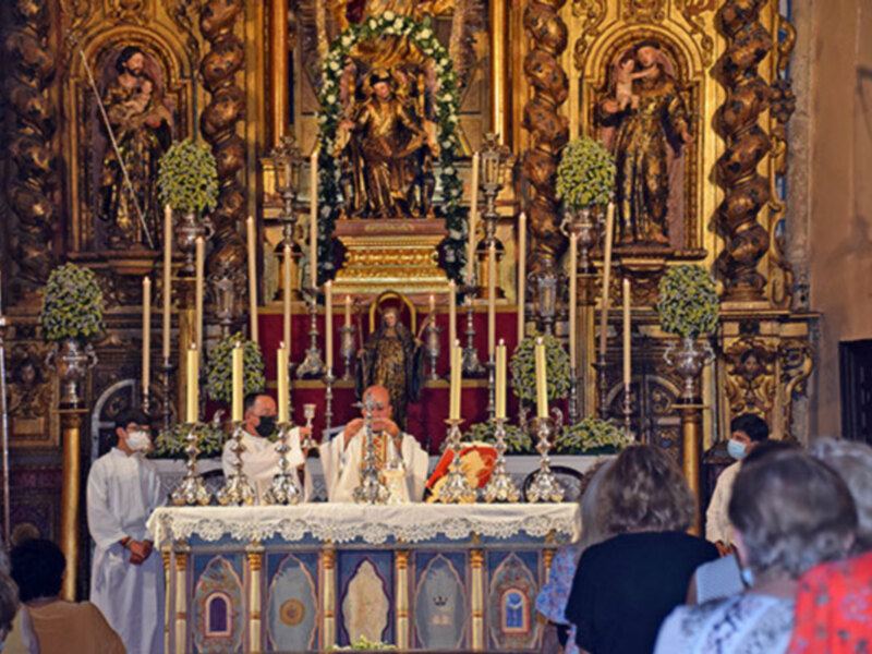 Sacerdotes oficiales una ceremonia religiosa en un altar adornado con flores y velas, con una imagen de la Virgen en el centro.