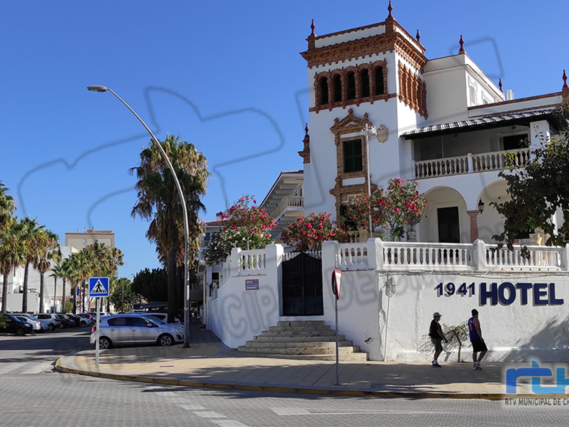 Hotel 1941 ubicado en la esquina de una calle con palmeras y edificios a lo lejos.