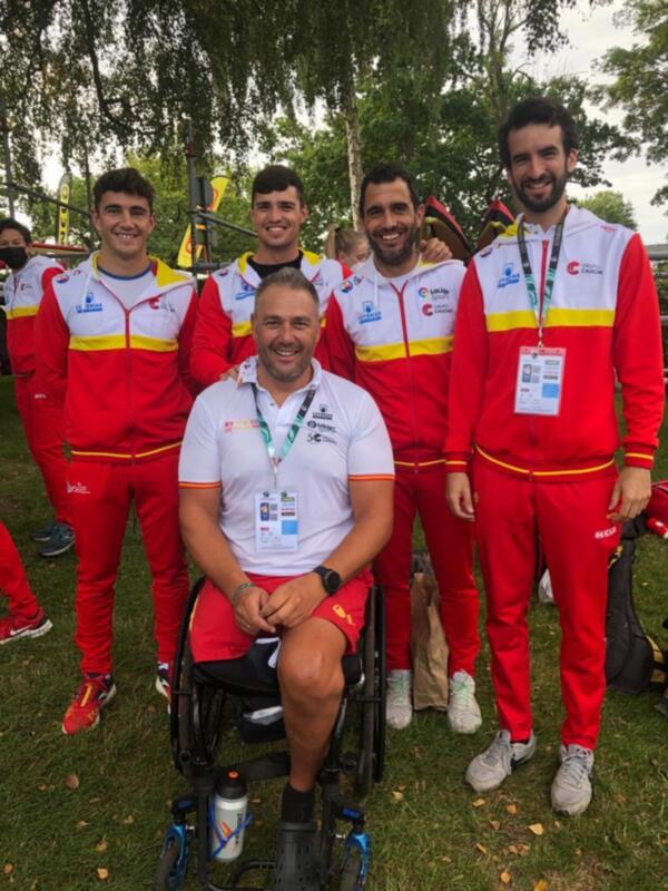 Equipo español de atletismo paralímpico posando en un evento deportivo al aire libre. El equipo está vestido con uniformes rojos y blancos con detalles en amarillo, y algunos miembros llevan etiquetas identificativas de la organización.