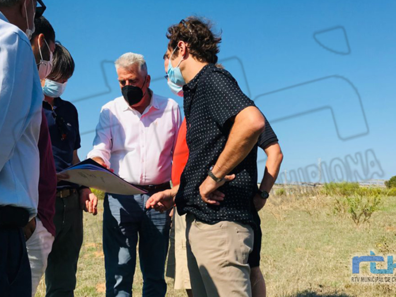 Grupo de personas en una reunión al aire libre, con un hombre en el centro llevando un documento y otros dos a su lado, todos con mascarillas. El contexto sugiere un ambiente de trabajo o negociación.