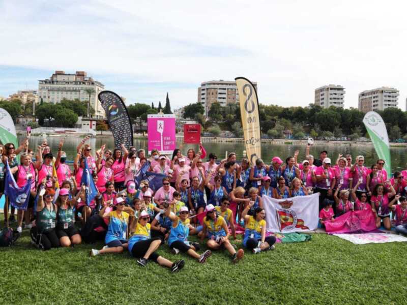 Equipo de atletas celebrando juntos en una carrera de fondo, con banderas y medallas, en un parque junto a un lago.