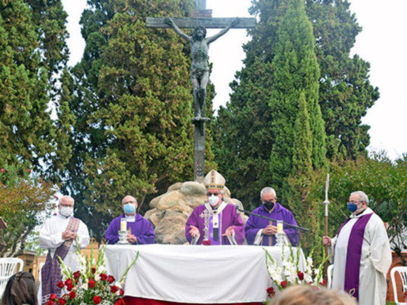 Especialistas en salud pública y religiosos participaron en una ceremonia religiosa en un cementerio, con máscaras y vestimenta litúrgica, frente a una estatua de Cristo crucificado.