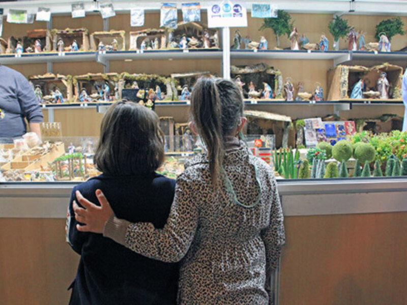 Dos personas abrazándose frente a una vitrina con figuras de navidad y plantas en el fondo.
