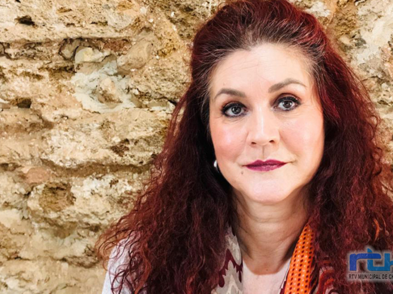 Una mujer con cabello rojo y una sonrisa en frente de una pared de ladrillo.