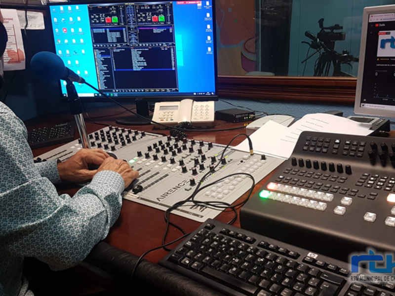 Un profesional de la radio o TV trabaja en un estudio con dos monitores, un micrófono, un teclado y un controlador de mezcla.
