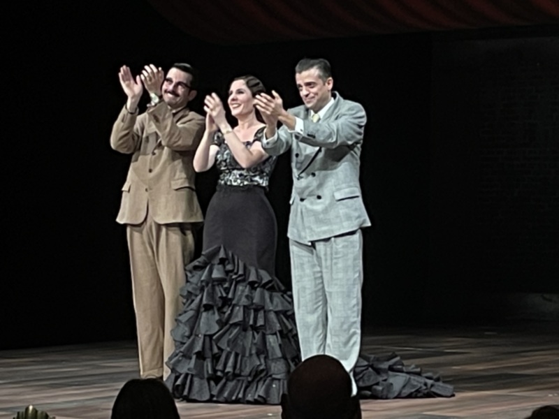 Tres personas saludando en una escena teatral, posiblemente en un espectáculo de flamenco o danza española.