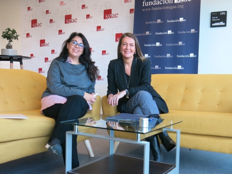 Dos personas sentadas en un sofá amarillo frente a un fondo con la marca 'SGAE' y una mesa con documentos. La imagen parece ser de una conferencia o evento empresarial.
