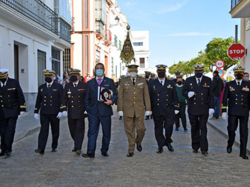 Personal militar desfilando en uniforme, con máscaras faciales, frente a edificios y árboles.