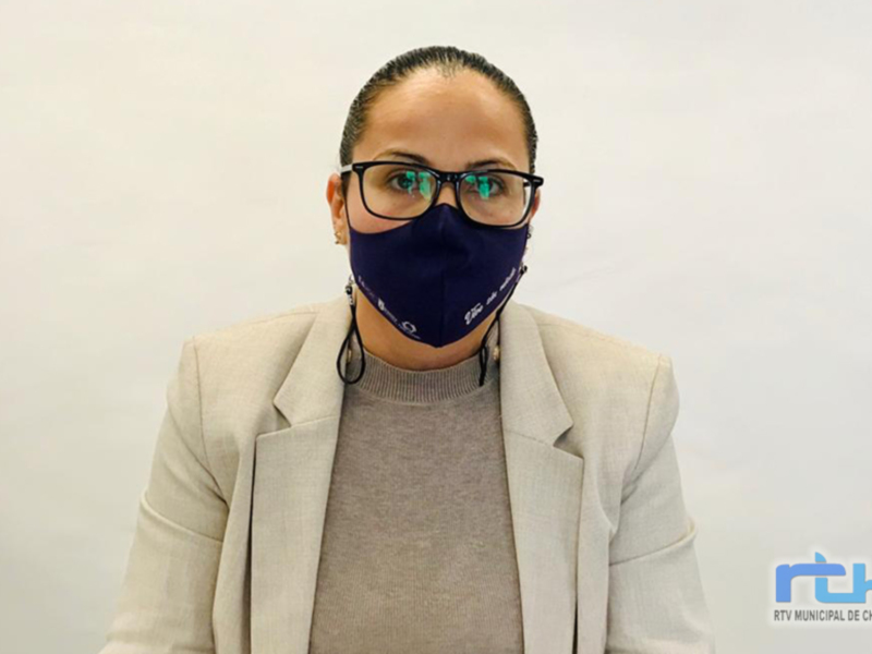 Una mujer con una máscara de protección facial azul con la letra "R" en letras blancas, un blazer beige y una camisa de color claro. La imagen tiene el logotipo "RTV.MUNICIPAL.DE.CHIPONA" en la esquina inferior derecha.