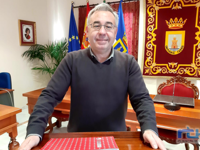 Un hombre en una oficina con una bandera y un escudo de armas en el fondo, posiblemente un político o funcionario público en España.