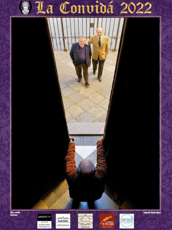 Dos hombres caminan por una puerta de hierro, con una perspectiva desde abajo hacia arriba, en un entorno urbano con azulejos y una estructura metálica.