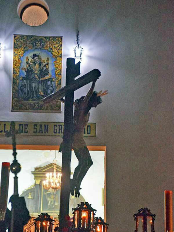 Cristo crucificado en una iglesia, con faroles y un cuadro religioso en el fondo.