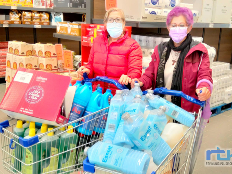 Dos personas con mascarillas en un supermercado, una con un carrito lleno de productos.