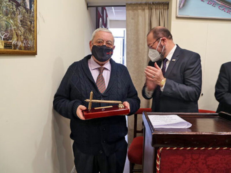 Celebración de un reconocimiento con una insignia de madera y un diploma en una ceremonia formal.