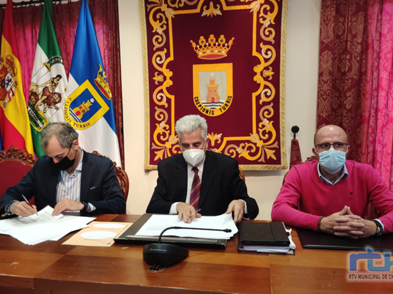 Firmas de acuerdo en una sala con banderas y un escudo de armas en el fondo.