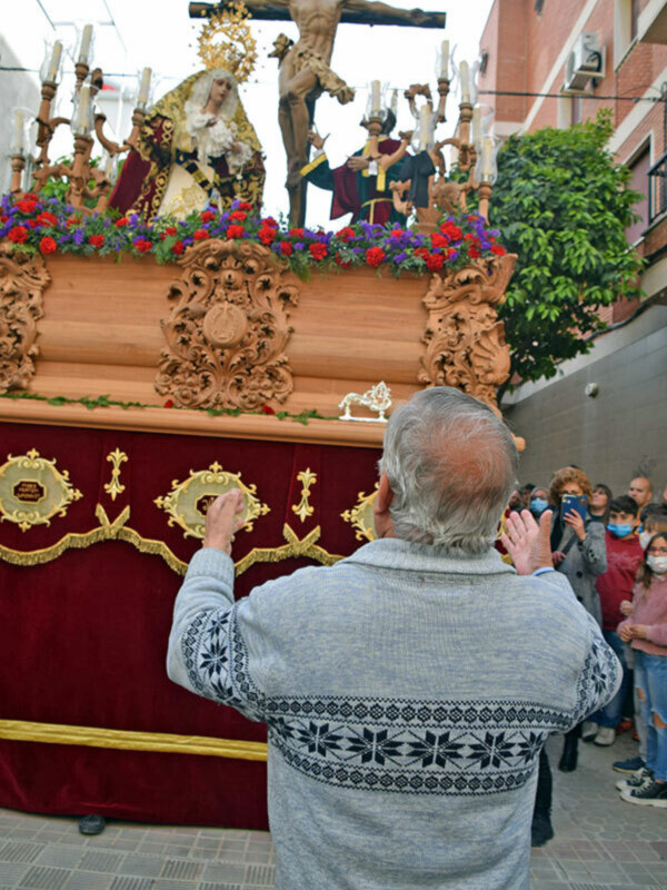 Fiesta religiosa con procesión de imágenes de Jesús y la Virgen, rodeadas de flores y acompañadas por fieles rezando.