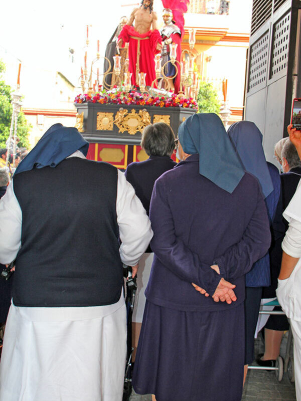 Una procesión religiosa con una imagen de Cristo en la cruz, acompañado por figuras históricas. Las personas presentes observan con atención el evento.
