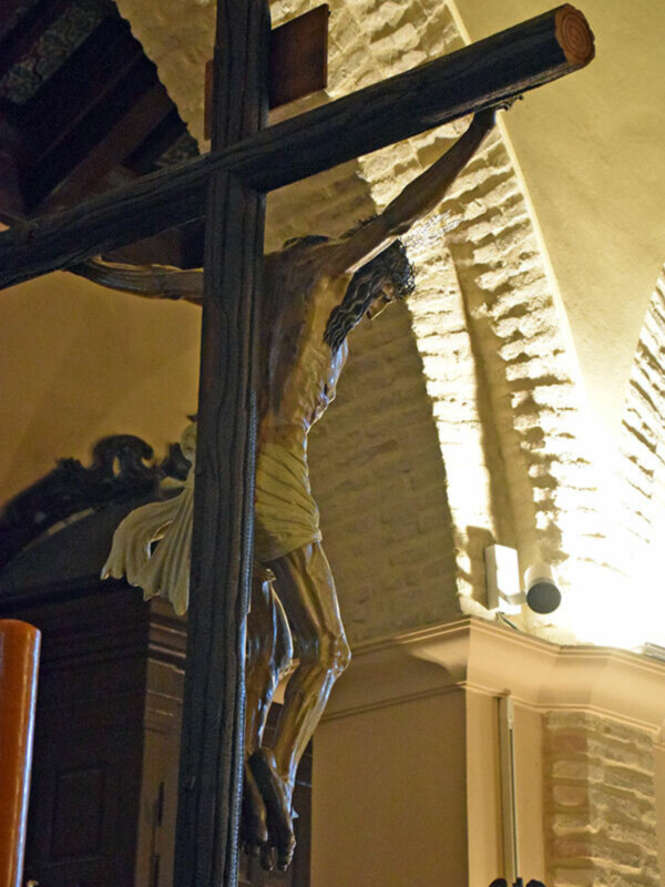 Crucifijo de madera en una iglesia, con luz proyectando sombras en el muro de ladrillos.
