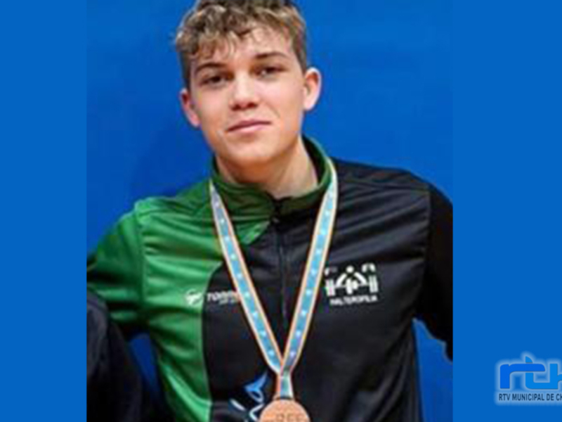 Un joven con una medalla de oro en el cuello, posando con orgullo frente a un fondo azul.