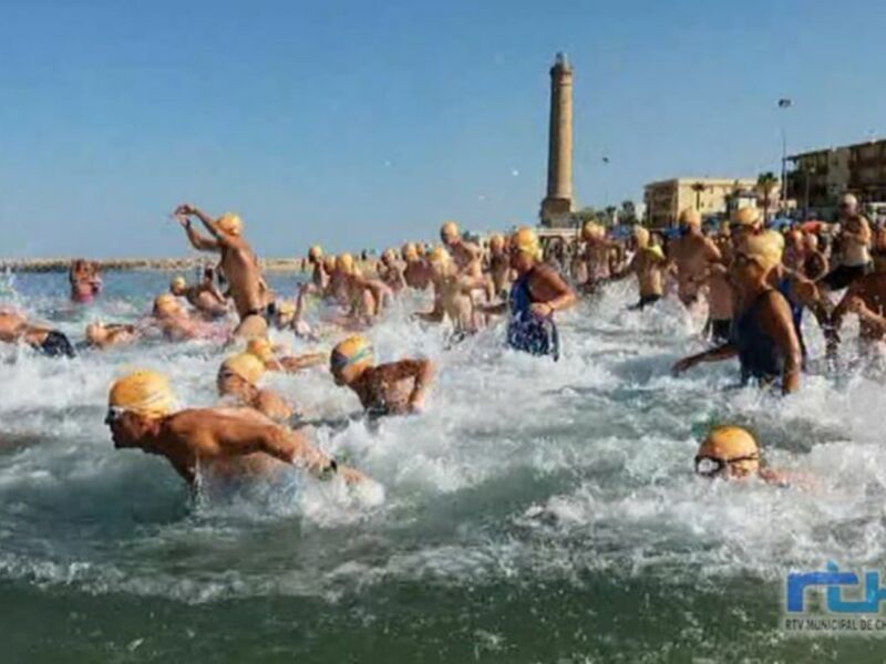 Gente nadando en el mar con una torre en el fondo, probablemente durante una competencia de natación.