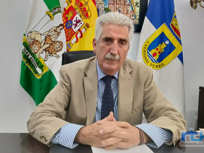 El alcalde de Chipiona, Antonio Sánchez, durante una comparecencia ante la prensa. Fondo con las banderas de la ciudad y la Junta de Andalucía.