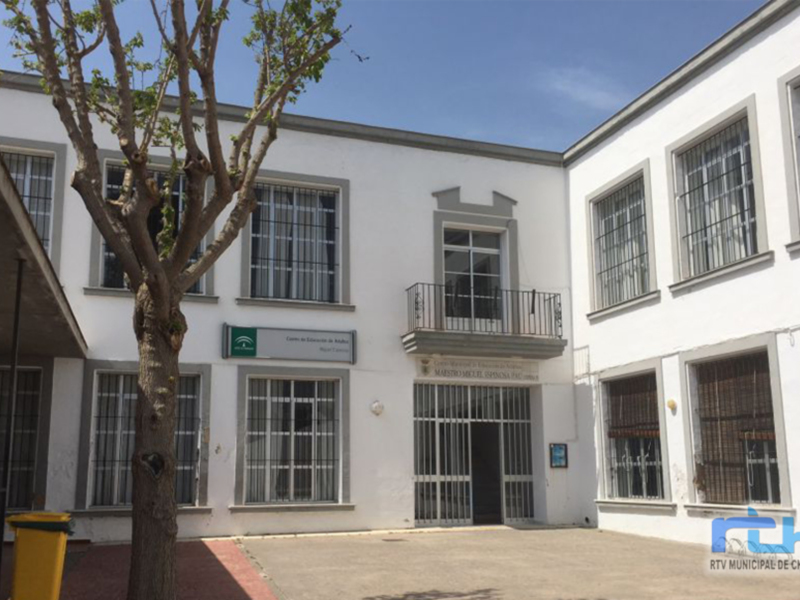 Edificio blanco con ventanas y puertas metálicas, árbol en el frente.