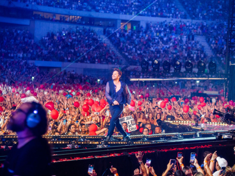 Artista en concierto con fanáticos entusiasmados sosteniendo globos rojos.